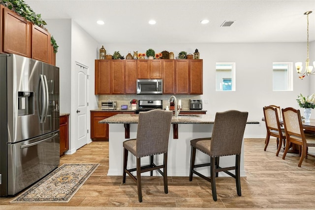 1559 Bayfront Park Aly, Winter Garden, FL 34787 - kitchen featuring appliances with stainless steel finishes, light wood-style floors, a kitchen breakfast bar, brown cabinets, and backsplash