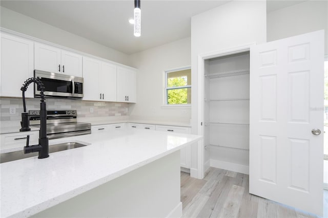 2011 W Tacoma Dr, Citrus Springs, FL 34434 - kitchen with appliances with stainless steel finishes, white cabinetry, light stone countertops, light wood-type flooring, and hanging light fixtures
