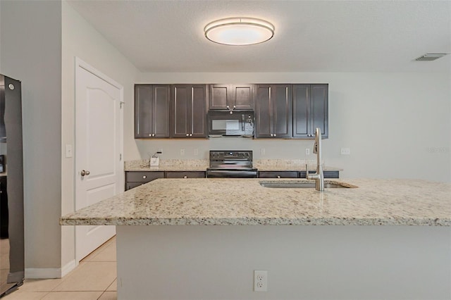 12104 Fawn Brindle St, Riverview, FL 33578 - kitchen featuring black appliances, light tile patterned floors, dark brown cabinetry, light stone counters, and a kitchen island with sink