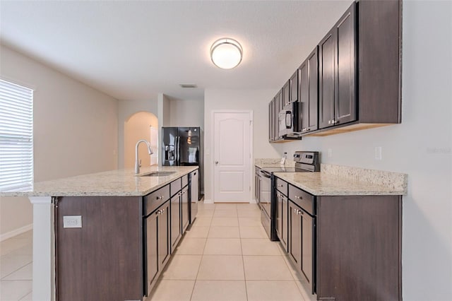 12104 Fawn Brindle St, Riverview, FL 33578 - kitchen with electric stove, light tile patterned flooring, arched walkways, dark brown cabinets, and stainless steel microwave