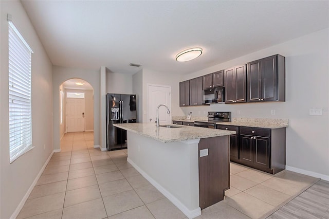12104 Fawn Brindle St, Riverview, FL 33578 - kitchen featuring black appliances, light tile patterned flooring, arched walkways, dark brown cabinets, and an island with sink