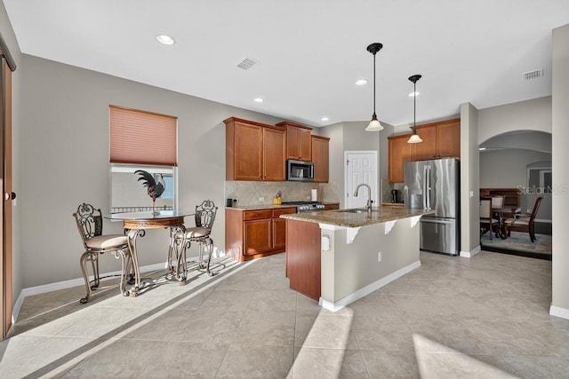 30120 Hackney Loop, Mount Dora, FL 32757 - kitchen featuring stainless steel appliances, arched walkways, light stone countertops, brown cabinetry, and backsplash