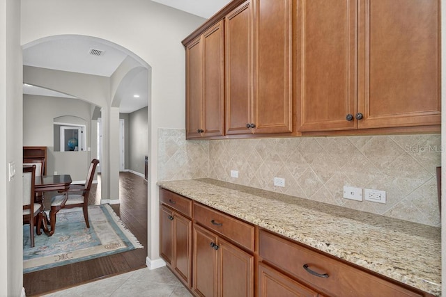 30120 Hackney Loop, Mount Dora, FL 32757 - kitchen with arched walkways, light stone countertops, backsplash, and brown cabinets