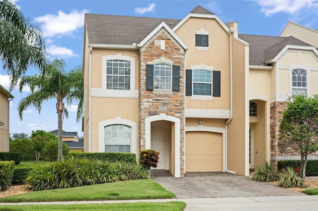 1011 Wood Cv, Kissimmee, FL 34743 - view of front facade featuring stone siding, stucco siding, decorative driveway, an attached garage, and a shingled roof