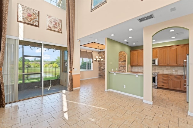 1011 Wood Cv, Kissimmee, FL 34743 - kitchen featuring stainless steel appliances, backsplash, brown cabinetry, arched walkways, and a chandelier