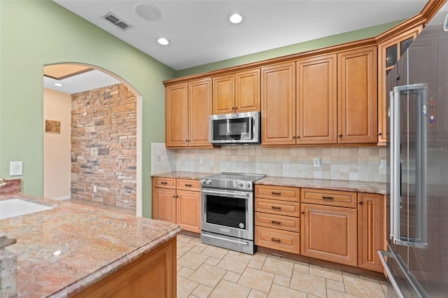 1011 Wood Cv, Kissimmee, FL 34743 - kitchen featuring appliances with stainless steel finishes, arched walkways, backsplash, light stone counters, and recessed lighting