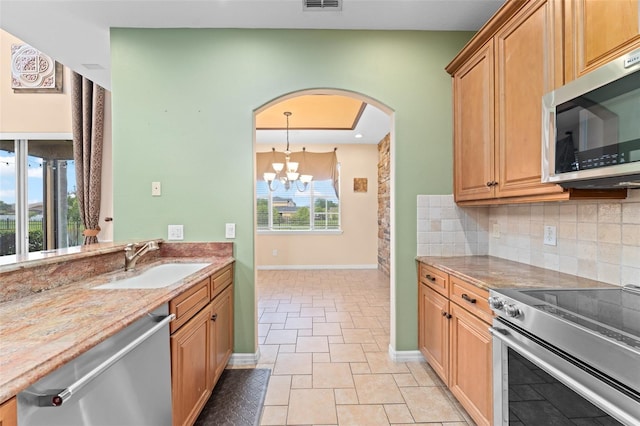 1011 Wood Cv, Kissimmee, FL 34743 - kitchen featuring stainless steel appliances, tasteful backsplash, a chandelier, light stone counters, and arched walkways