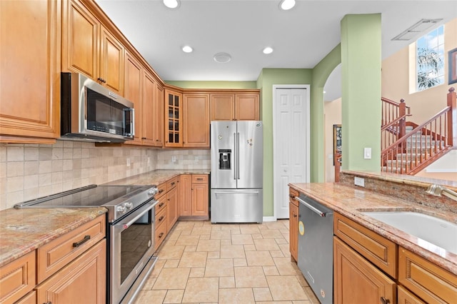 1011 Wood Cv, Kissimmee, FL 34743 - kitchen with stainless steel appliances, stone tile floors, arched walkways, tasteful backsplash, and light stone countertops