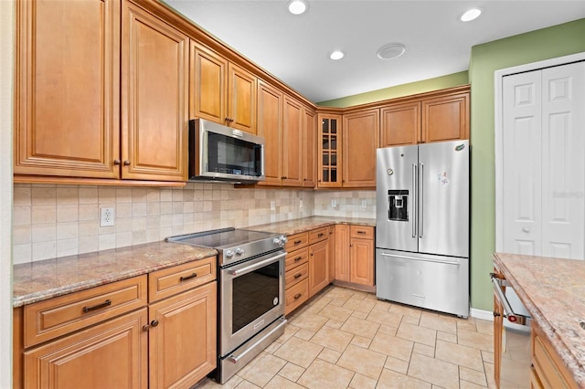 1011 Wood Cv, Kissimmee, FL 34743 - kitchen with appliances with stainless steel finishes, decorative backsplash, light stone countertops, glass insert cabinets, and recessed lighting