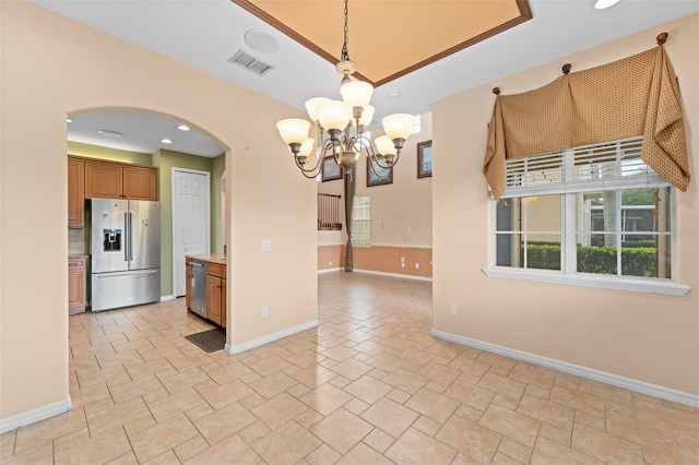 1011 Wood Cv, Kissimmee, FL 34743 - kitchen featuring appliances with stainless steel finishes, arched walkways, a chandelier, brown cabinetry, and light stone finish floors