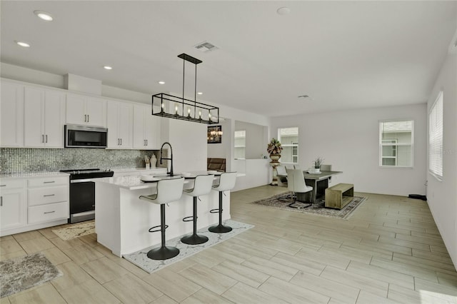 2912 Sanctuary Dr, Clermont, FL 34714 - kitchen with appliances with stainless steel finishes, decorative backsplash, a kitchen island with sink, light countertops, and white cabinetry