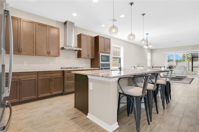 1564 Atlantic Coastline Loop, Oakland, FL 34787 - kitchen featuring wall chimney range hood, appliances with stainless steel finishes, an island with sink, light wood finished floors, and tasteful backsplash