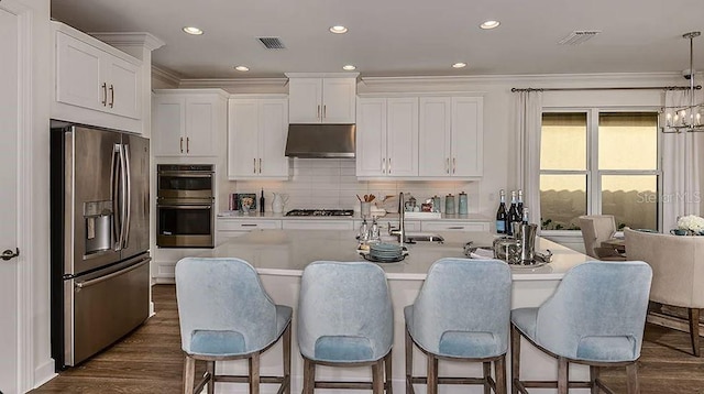 858 Arbor Green Trl, Saint Cloud, FL 34771 - kitchen featuring appliances with stainless steel finishes, under cabinet range hood, light countertops, white cabinets, and a kitchen breakfast bar