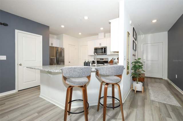 2326 Carrabelle Way, Sanford, FL 32771 - kitchen with appliances with stainless steel finishes, light wood-style floors, white cabinetry, a kitchen bar, and recessed lighting