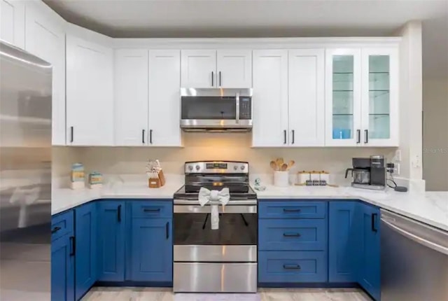 365 Aylesbury Ct, Kissimmee, FL 34758 - kitchen featuring appliances with stainless steel finishes, light countertops, white cabinetry, glass insert cabinets, and blue cabinetry