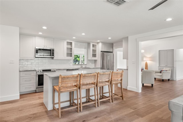 91 Minnehaha Cir, Maitland, FL 32751 - kitchen with stainless steel appliances, a breakfast bar area, glass insert cabinets, light wood-type flooring, and tasteful backsplash