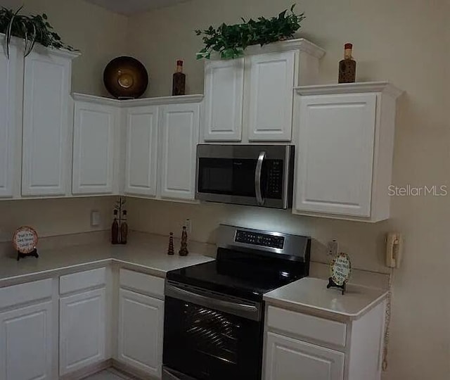 37 Ethan Allen Dr, Palm Coast, FL 32164 - kitchen with stainless steel microwave, range with electric cooktop, light countertops, and white cabinetry