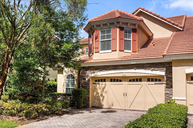 7348 Regina Way, Orlando, FL 32819 - view of front of property featuring stone siding, stucco siding, decorative driveway, a tiled roof, and an attached garage