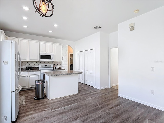 799 Hacienda Cir, Kissimmee, FL 34741 - kitchen with white appliances, a center island, arched walkways, dark wood-style floors, and white cabinetry
