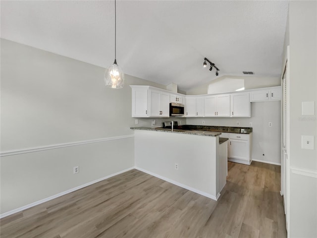 101 Whitley Bay Ln, Longwood, FL 32779 - kitchen with stainless steel microwave, vaulted ceiling, dark countertops, white cabinetry, and light wood finished floors