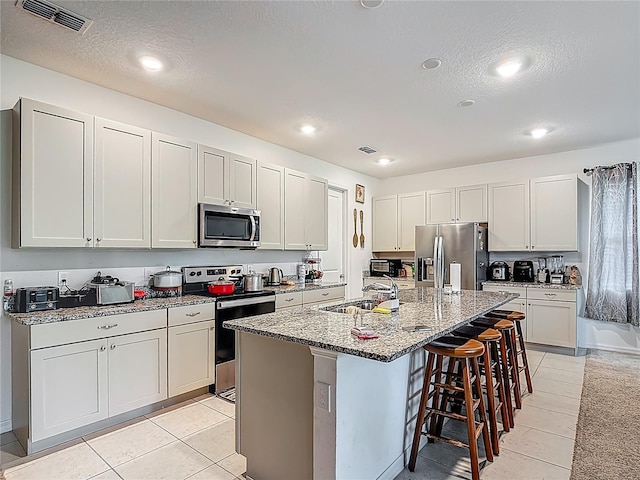 711 Steerview St, Saint Cloud, FL 34771 - kitchen with appliances with stainless steel finishes, a kitchen bar, light stone countertops, a center island with sink, and light tile patterned floors