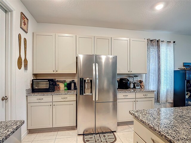 711 Steerview St, Saint Cloud, FL 34771 - kitchen with stainless steel fridge, light stone countertops, light tile patterned flooring, a textured ceiling, and white cabinetry