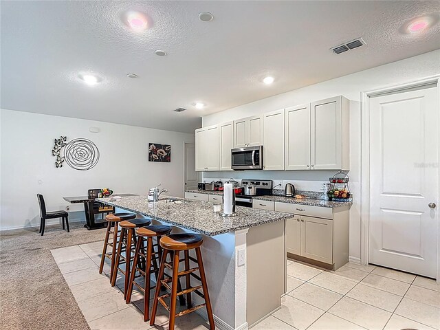 711 Steerview St, Saint Cloud, FL 34771 - kitchen featuring appliances with stainless steel finishes, a kitchen bar, a center island with sink, light stone countertops, and a textured ceiling