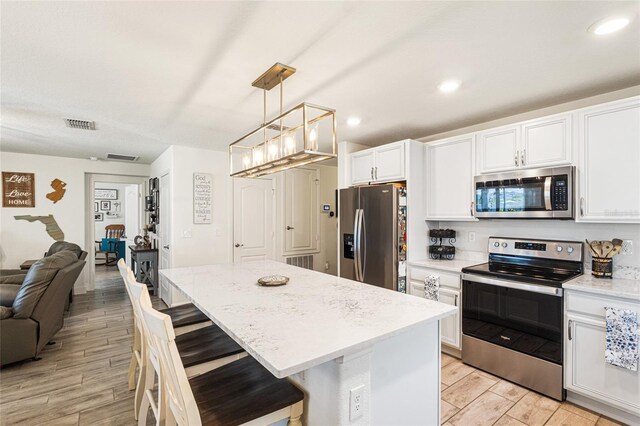 1668 Wilson Prairie Cir, Groveland, FL 34736 - kitchen featuring appliances with stainless steel finishes, open floor plan, white cabinetry, light wood-type flooring, and a breakfast bar