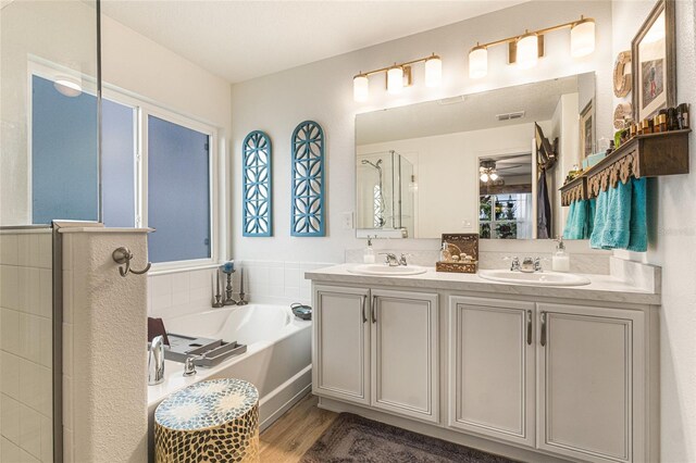 1668 Wilson Prairie Cir, Groveland, FL 34736 - full bath featuring double vanity, a bath, a shower stall, wood finished floors, and a ceiling fan
