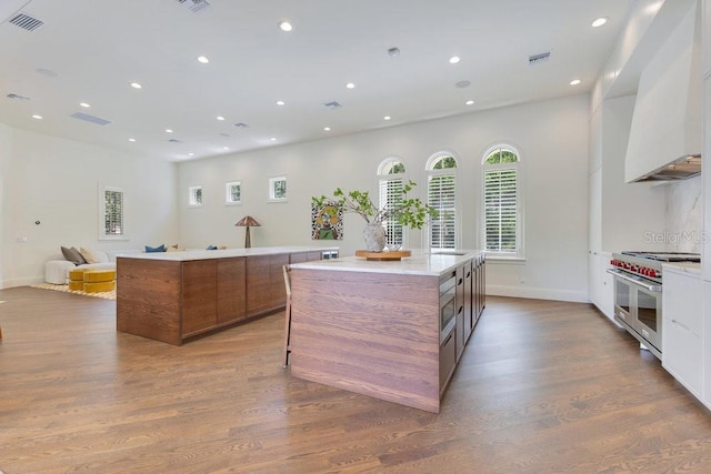 6186 Louise Cove Dr, Windermere, FL 34786 - kitchen featuring range with two ovens, a spacious island, brown cabinetry, custom exhaust hood, and dark wood-style flooring