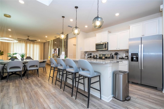 1907 Summer Dr, Davenport, FL 33897 - kitchen with stainless steel appliances, light wood-style flooring, a ceiling fan, tasteful backsplash, and white cabinetry