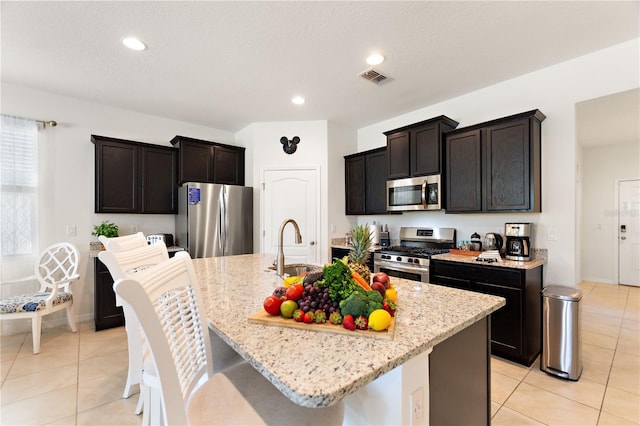8020 Oak Shadow Ct, Davenport, FL 33837 - kitchen featuring appliances with stainless steel finishes, light stone countertops, light tile patterned floors, a kitchen island with sink, and a breakfast bar area