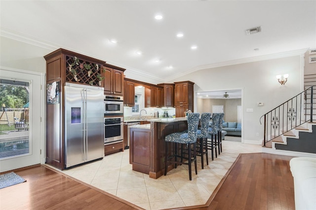 8445 Shady Glen Dr, Orlando, FL 32819 - kitchen with stainless steel appliances, ornamental molding, a kitchen bar, light stone countertops, and light wood-style flooring