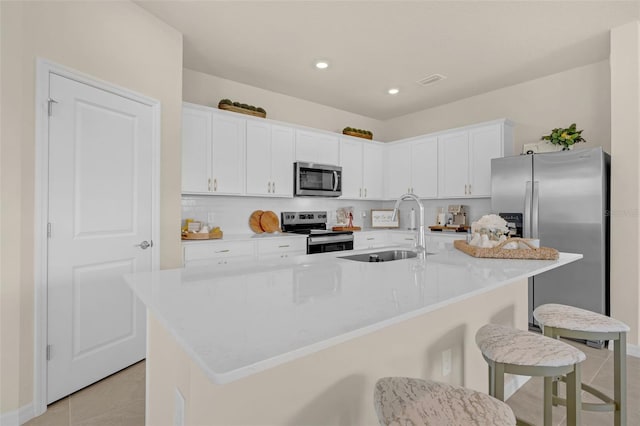 3702 Haddon Ave, Davenport, FL 33837 - kitchen featuring appliances with stainless steel finishes, a breakfast bar area, light tile patterned floors, white cabinets, and a center island with sink