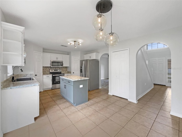 1301 Brenway Dr, Mascotte, FL 34753 - kitchen with appliances with stainless steel finishes, arched walkways, light tile patterned floors, white cabinetry, and a kitchen island