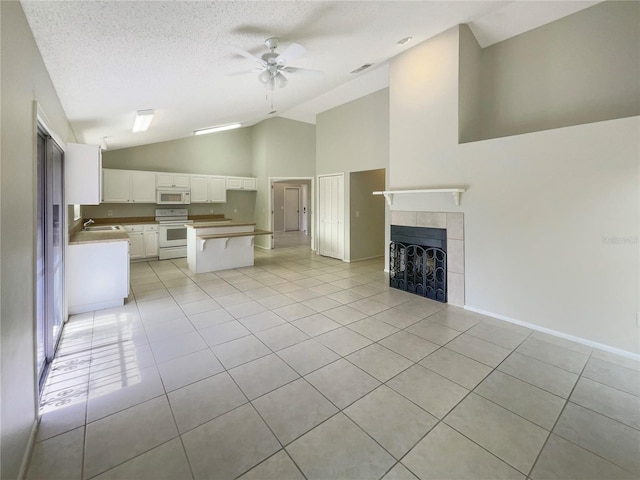 6460 Preakness Dr, Orlando, FL 32818 - unfurnished living room featuring vaulted ceiling, light tile patterned floors, a ceiling fan, a tiled fireplace, and a textured ceiling
