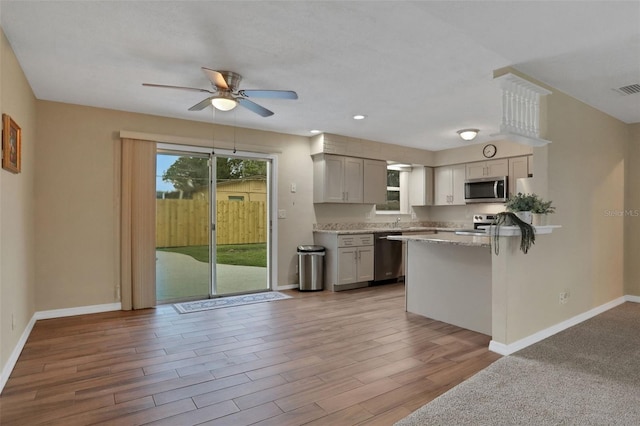 749 Ridge Blvd, South Daytona, FL 32119 - kitchen with appliances with stainless steel finishes, ceiling fan, wood finished floors, a peninsula, and light stone countertops