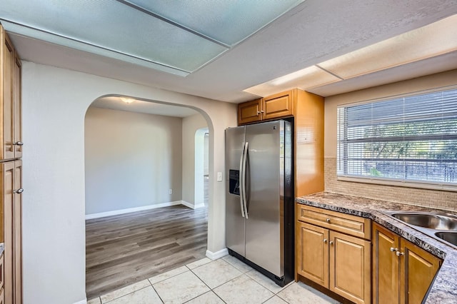 1175 Tracy Dr, Port Orange, FL 32129 - kitchen with stainless steel fridge with ice dispenser, arched walkways, light tile patterned flooring, brown cabinetry, and tasteful backsplash