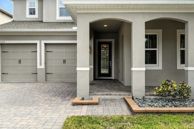 15315 Gilligan Ct, Winter Garden, FL 34787 - doorway to property featuring stucco siding, decorative driveway, an attached garage, and a shingled roof