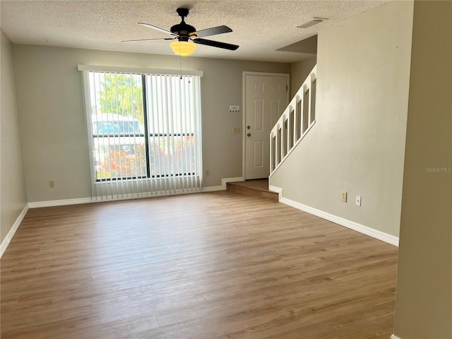 unfurnished living room with wood finished floors, a ceiling fan, a textured ceiling, and stairs