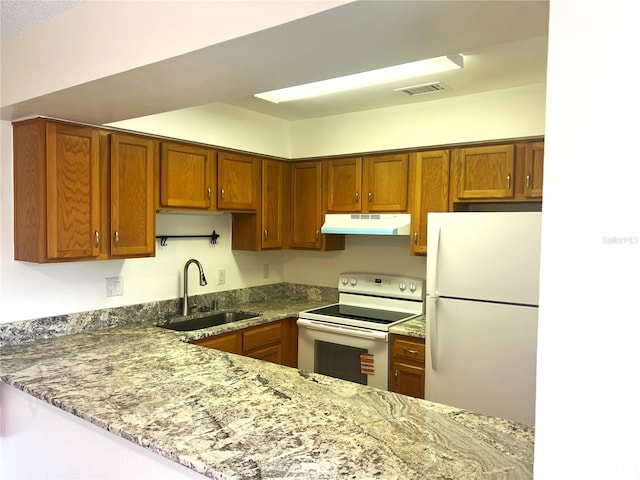 kitchen with white appliances, under cabinet range hood, brown cabinetry, and stone counters