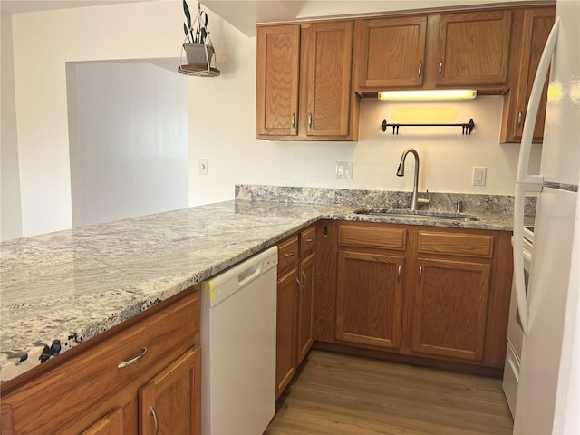 kitchen with white appliances, brown cabinets, light wood-style flooring, and light stone counters