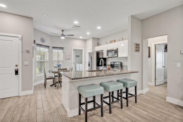 4636 Piedmont St, Orlando, FL 32811 - kitchen featuring appliances with stainless steel finishes, white cabinets, a kitchen breakfast bar, light wood-type flooring, and recessed lighting
