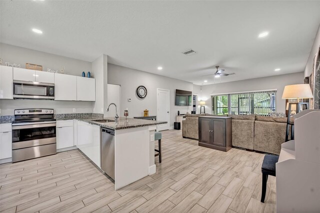 4636 Piedmont St, Orlando, FL 32811 - kitchen featuring stainless steel appliances, white cabinets, a peninsula, ceiling fan, and dark stone counters