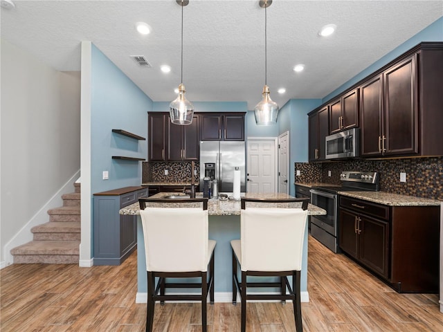2556 Ocoee Reserve Ct, Ocoee, FL 34761 - kitchen with appliances with stainless steel finishes, open shelves, dark brown cabinets, an island with sink, and a textured ceiling