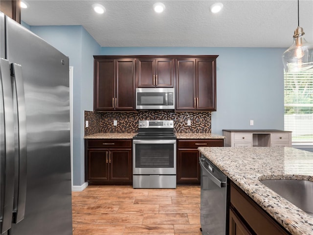 2556 Ocoee Reserve Ct, Ocoee, FL 34761 - kitchen featuring stainless steel appliances, dark brown cabinets, light wood-type flooring, light stone countertops, and tasteful backsplash