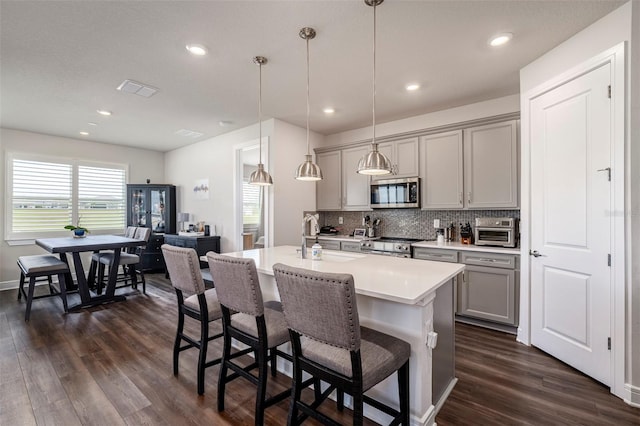 7484 Catania Loop, Clermont, FL 34714 - kitchen with stainless steel microwave, gray cabinets, dark wood-style floors, backsplash, and a breakfast bar