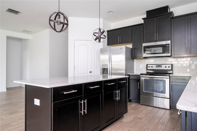 15586 Hamlin Blossom Ave, Winter Garden, FL 34787 - kitchen featuring stainless steel appliances, dark cabinets, decorative backsplash, light wood-style flooring, and a kitchen island