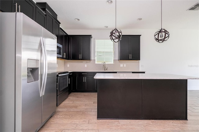 15586 Hamlin Blossom Ave, Winter Garden, FL 34787 - kitchen with stainless steel appliances, a kitchen island, light wood finished floors, dark cabinetry, and decorative backsplash