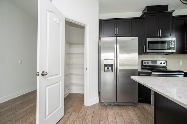 15586 Hamlin Blossom Ave, Winter Garden, FL 34787 - kitchen featuring appliances with stainless steel finishes, dark cabinetry, light wood finished floors, and decorative backsplash